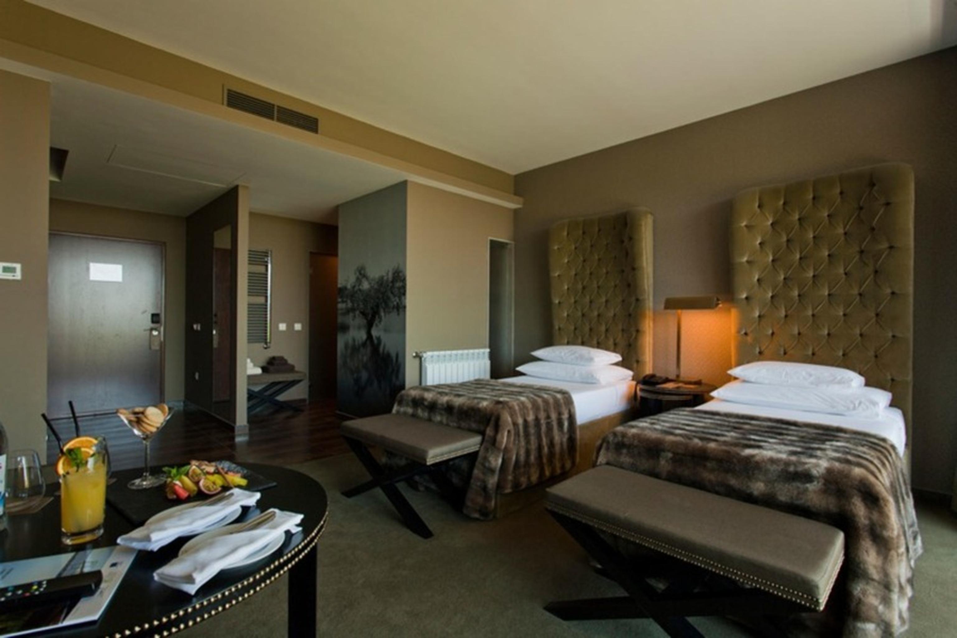 Ap Lago Montargil - Conference & Spa Exterior photo The photo shows a stylish hotel room featuring two beds with plush, upholstered headboards. The room has a modern and elegant design, with earthy tones dominating the decor. A small round table is set up in the foreground, displaying a drink and some